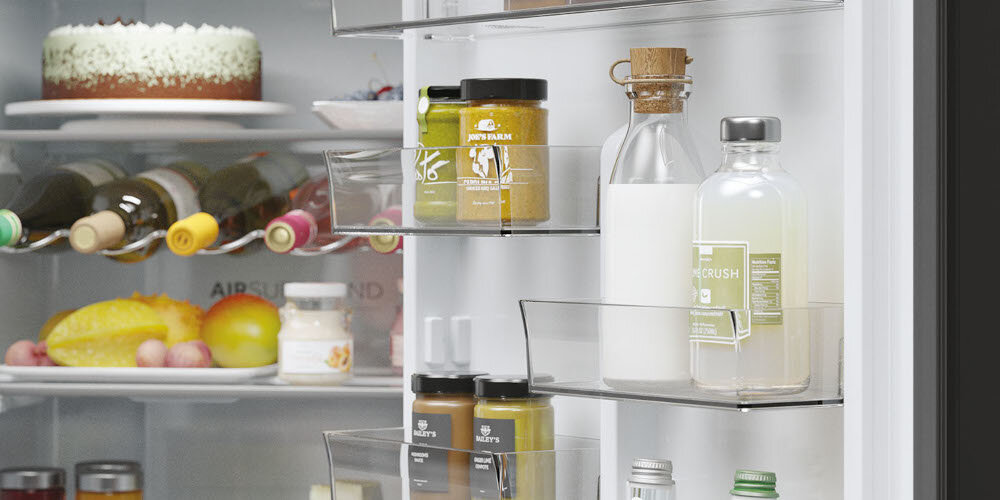 Wnętrze lodówki z widocznymi półkami, na których znajdują się różne produkty spożywcze, w tym butelki, słoiki i ciasto. Na drzwiach lodówki umieszczone są dodatkowe półki z napojami i przyprawami.
