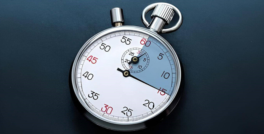 Na obrazie widoczny jest stoper z metalową obudową i białą tarczą. Na tarczy znajdują się czarne i czerwone cyfry oraz dwie wskazówki.