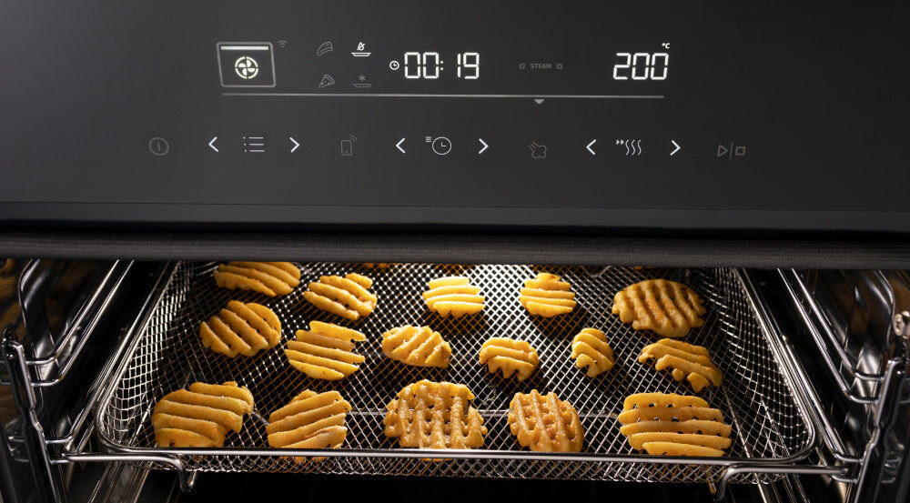 Piekarnik z wyświetlaczem pokazującym czas 00:19 i temperaturę 200°C. W środku piekarnika na ruszcie znajdują się pieczone ciasteczka.