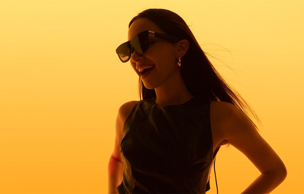 Okulary XREAL One Czarny prezentacja okularów założonych na kobiecie na żółtym tle odwrotne pole dźwiękowe realistyczne wrażenie przestrzeni nagrywanie stereo