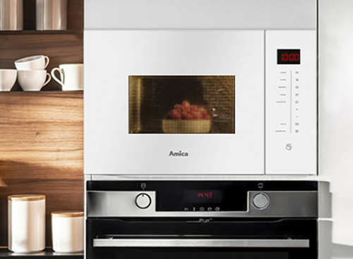 Biała kuchenka mikrofalowa z logo Amica, z wyświetlaczem pokazującym godzinę 10:00 i przyciskami po prawej stronie. Wewnątrz znajduje się miska z czerwonymi owocami.