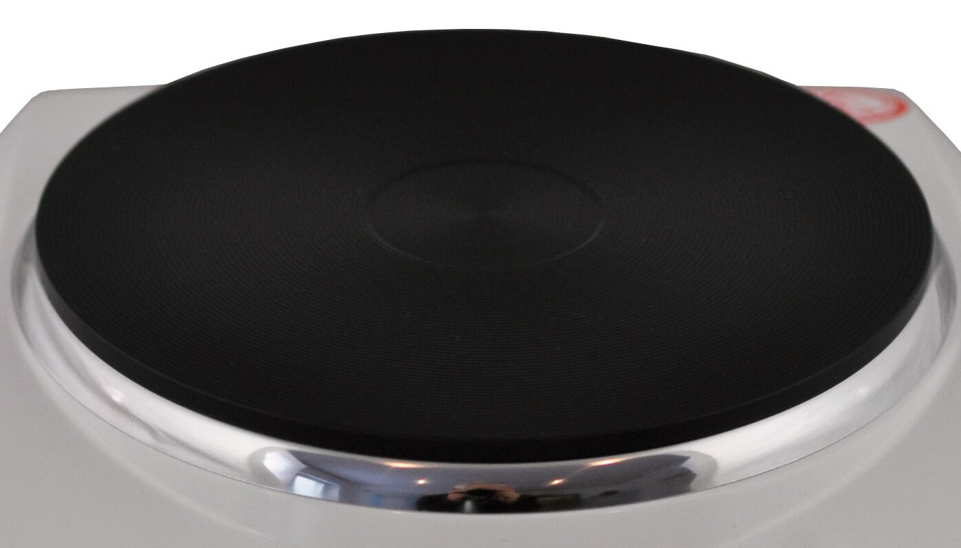 Obraz przedstawia czarną płytę grzewczą na białej podstawie, prawdopodobnie część kuchenki nastawnej. Widać także fragment czerwonego elementu w rogu.