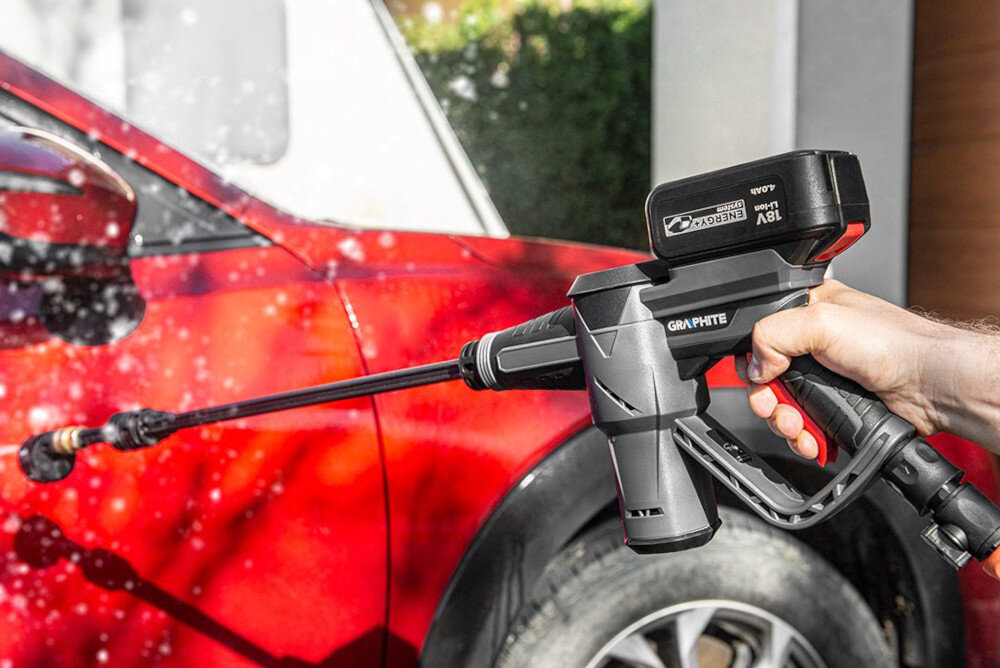 Osoba trzyma myjkę ciśnieniową GRAPHITE, która spryskuje wodą czerwony samochód. Na myjce widoczne jest logo \'GRAPHITE\' oraz napis \'Energy+\' na baterii.
