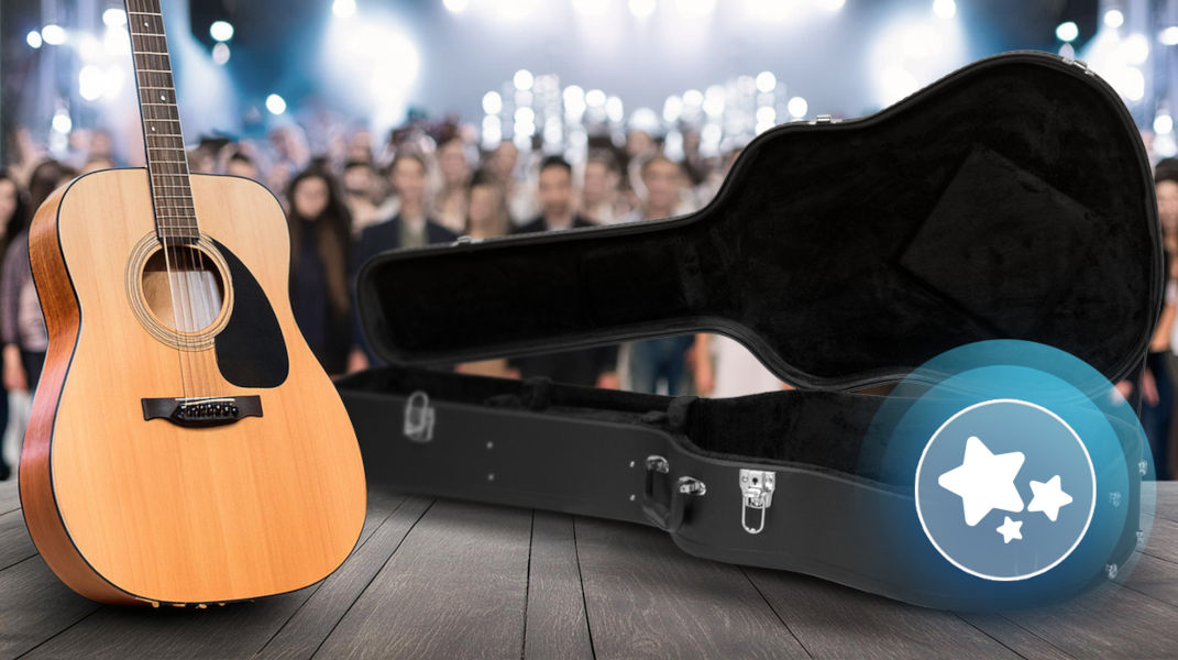 Na drewnianej podłodze stoi akustyczna gitara obok otwartego, czarnego futerału. W tle widać rozmytą publiczność i jasne światła sceniczne.