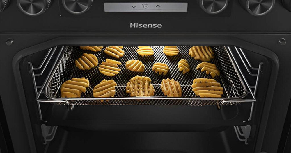 Otwarty piekarnik z logo Hisense, w którym na metalowej kratce znajdują się kawałki ciasta w kształcie frytek. Panel sterowania z pokrętłami i przyciskami widoczny jest nad komorą piekarnika.