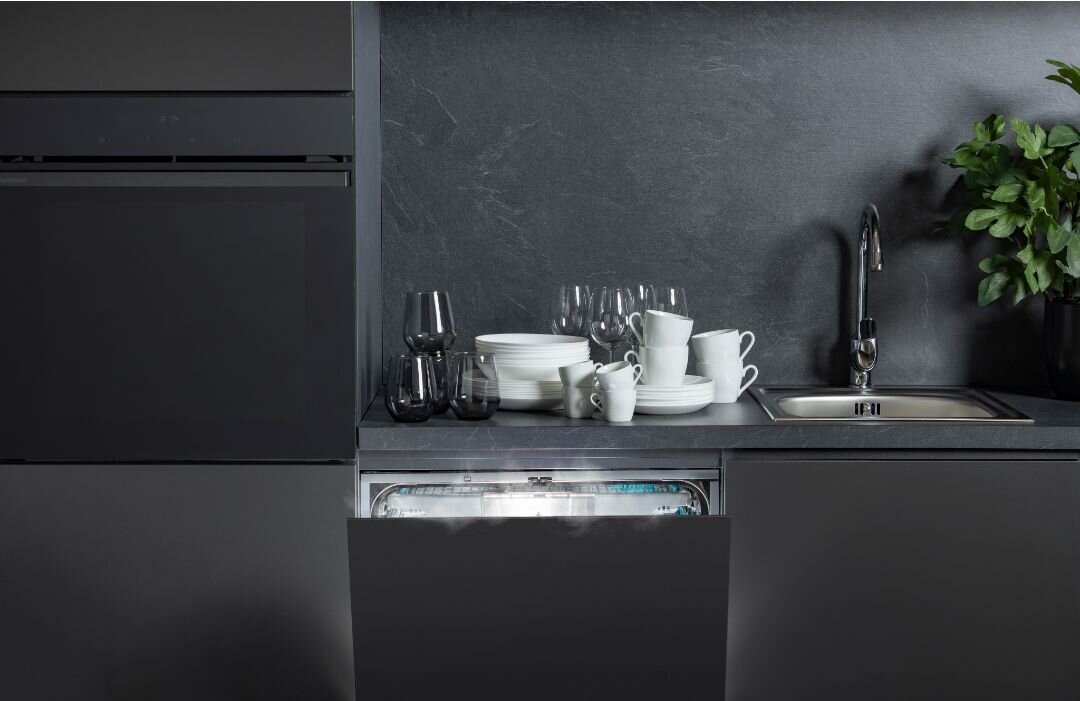 Kuchnia z otwartą zmywarką, na której widoczne są czyste naczynia. Obok znajduje się zlew i roślina w doniczce.