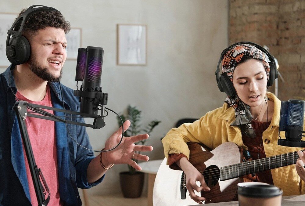 Mikrofon BOYA K3 Mężczyzna śpiewa do czarnego mikrofonu BOYA K3 z podświetleniem RGB, kobieta gra na gitarze akustycznej w tle, oboje w słuchawkach, opis