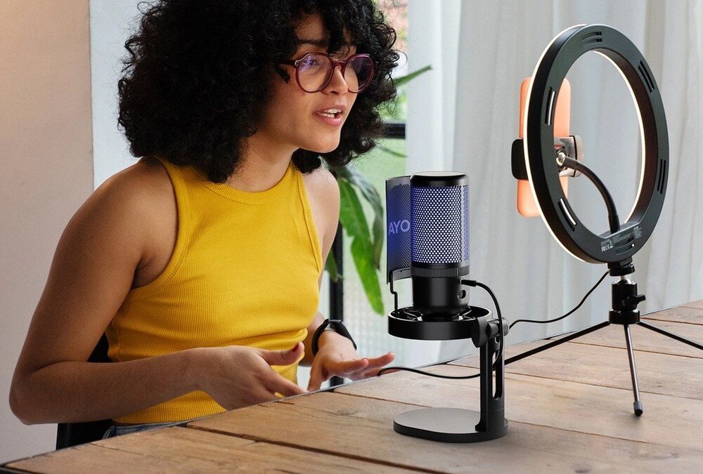 Mikrofon BOYA K3 Kobieta w żółtej koszulce nagrywa przy stoliku z mikrofonem BOYA K3 z niebieskim podświetleniem, obok ring light, jasne wnętrze z roślinami w tle, redukcja szumów, wyciszenie