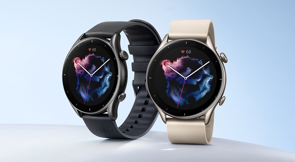 Dwa smartwatche z okrągłymi tarczami, jeden z ciemnym paskiem, drugi z jasnym. Na wyświetlaczach widoczny jest kolorowy wzór i ikona serca z liczbą \'68\'.
