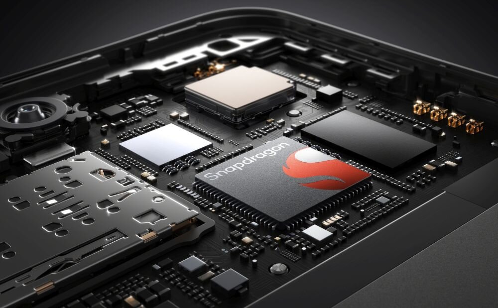Zdjęcie przedstawia wnętrze urządzenia elektronicznego z widocznym układem scalonym z napisem \'Snapdragon\'. Wokół układu znajdują się różne komponenty elektroniczne na płytce drukowanej.