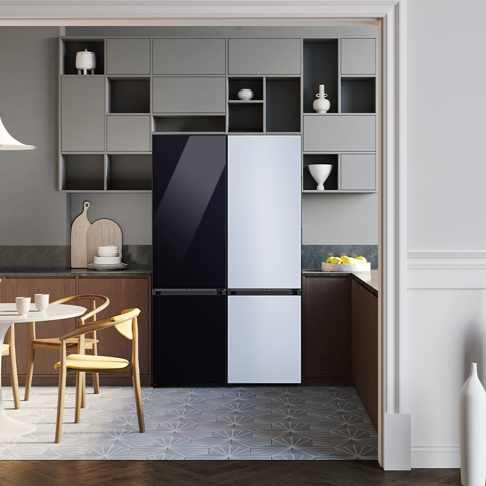 W kuchni znajduje się lodówka z czarnym i białym frontem, otoczona szarymi szafkami. Na blacie obok lodówki stoi misa z cytrynami.