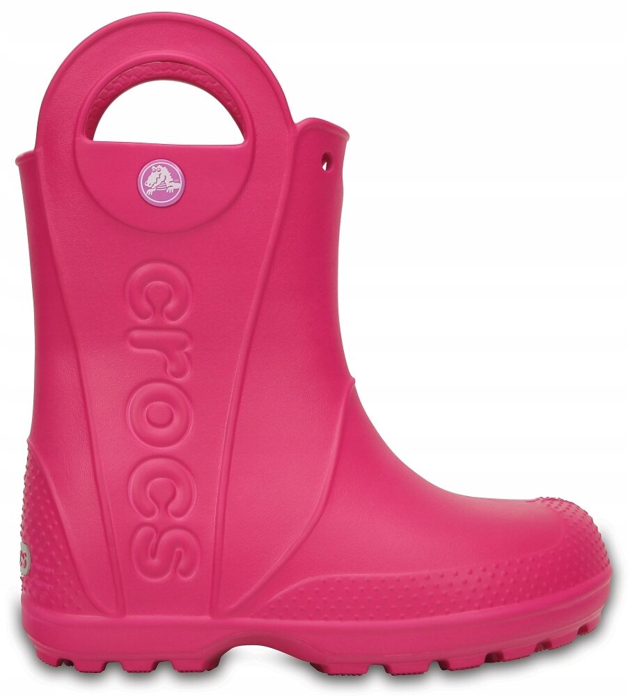 Różowy kalosz dziecięcy z dużym uchwytem na górze i napisem \'crocs\' wytłoczonym na boku. Na górze znajduje się okrągłe logo z białym krokodylem na fioletowym tle.