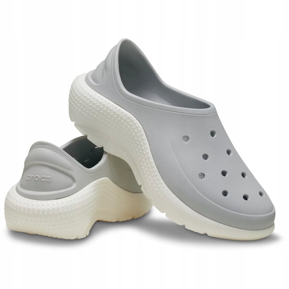Na obrazie widoczne są szare, wsuwane buty sportowe z perforacjami na wierzchu i białą podeszwą. Na jednym z butów znajduje się napis \'crocs\'.