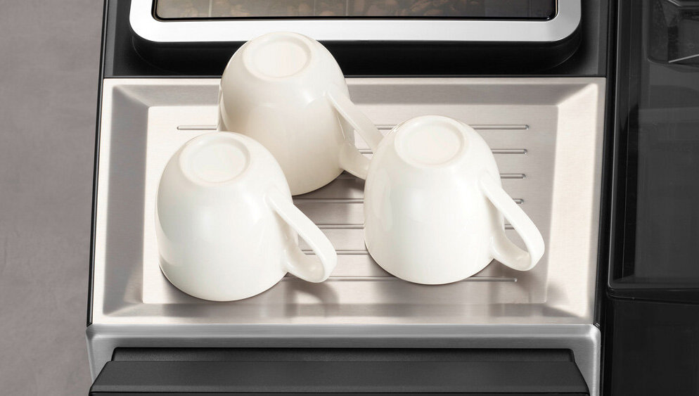 Na metalowej tacy znajdują się trzy odwrócone białe filiżanki. Taca jest częścią urządzenia kuchennego.