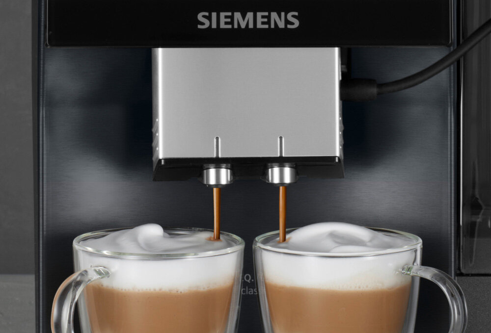 Ekspres do kawy marki SIEMENS przygotowuje dwa kubki kawy z mleczną pianką. Logo \'SIEMENS\' widoczne jest na górze urządzenia.
