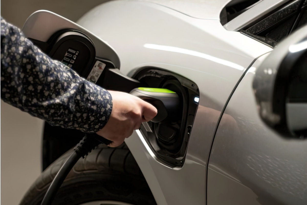 Osoba podłącza kabel do ładowania samochodu elektrycznego do gniazda w pojeździe. Kabel ma czarną obudowę z zielonym akcentem na końcówce.