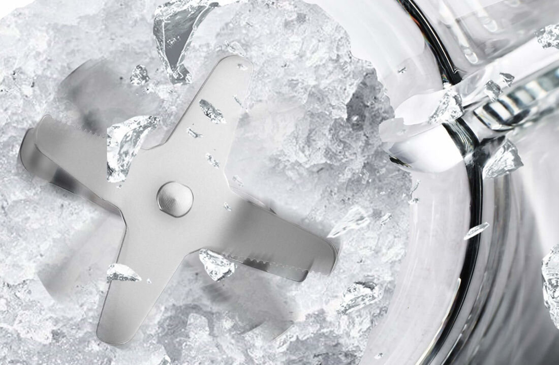Obraz przedstawia metalowe ostrze w ruchu, rozdrabniające lód w przezroczystym pojemniku. Widać rozpryskujące się kawałki lodu wokół ostrza.