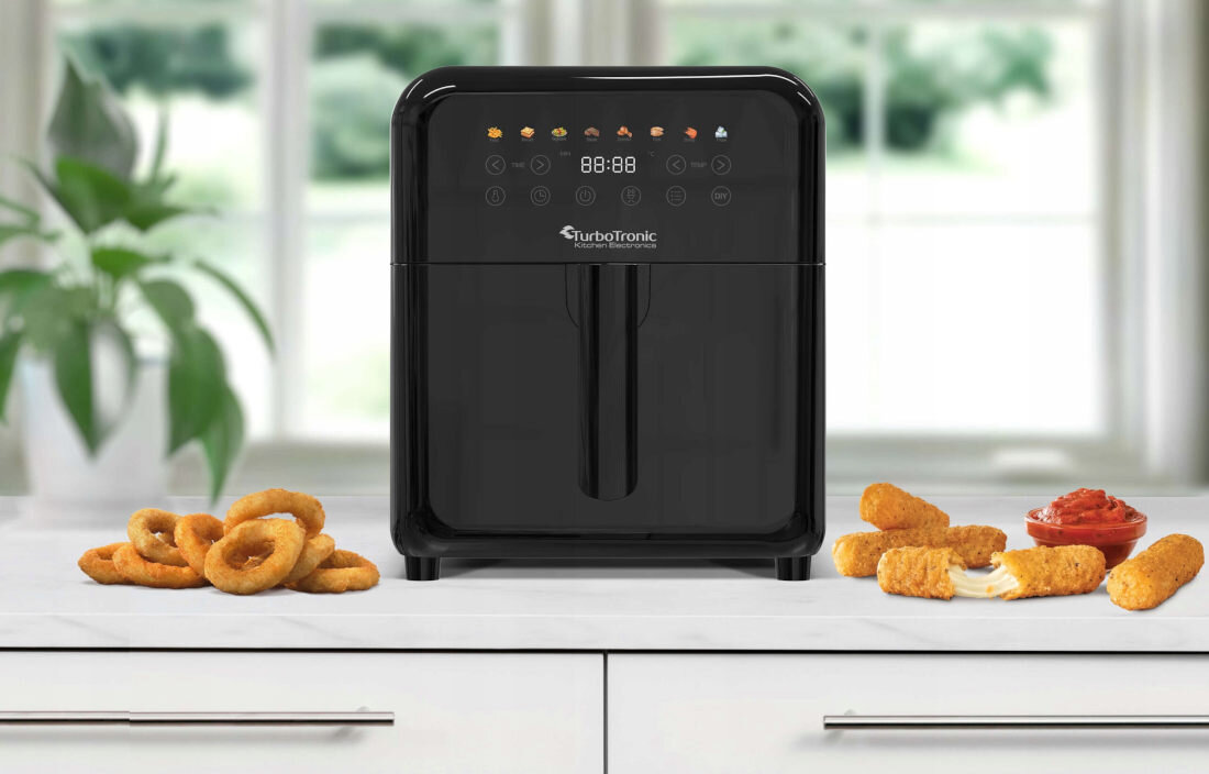 Czarna frytkownica beztłuszczowa TurboTronic z wyświetlaczem cyfrowym i przyciskami dotykowymi stoi na blacie kuchennym. Obok urządzenia znajdują się krążki cebulowe i panierowane przekąski z sosem.
