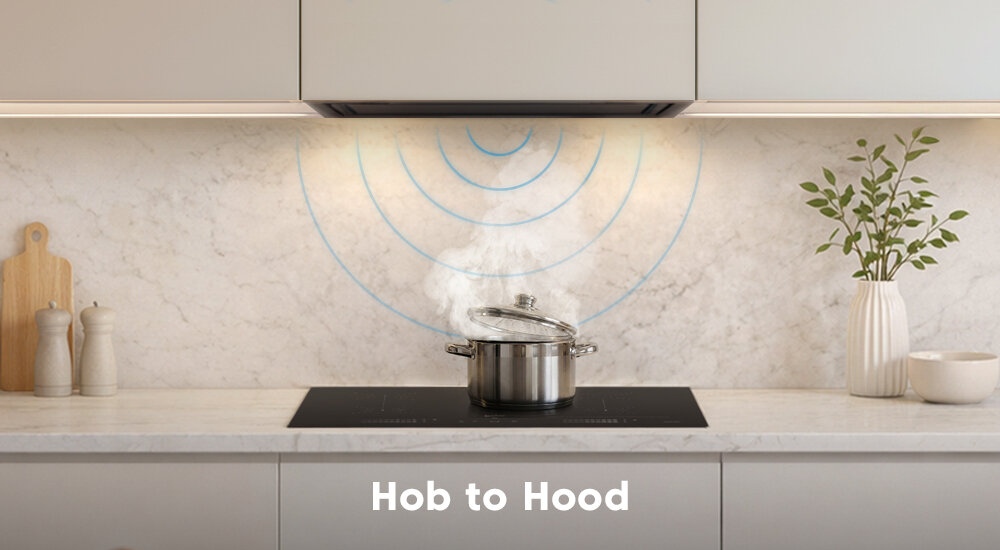 Na blacie kuchennym znajduje się płyta indukcyjna z garnkiem, z którego unosi się para. Na ścianie widoczny jest napis \'Hob to Hood\'.