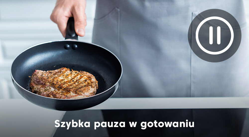 Osoba trzyma patelnię z kawałkiem mięsa nad płytą indukcyjną. Na obrazie widoczny jest tekst: \'Szybka pauza w gotowaniu\'.