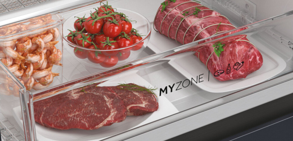Wnętrze lodówki z szufladą zawierającą różne produkty spożywcze: krewetki, pomidory koktajlowe w misce, surowe mięso i pieczeń. Na szufladzie widoczny jest napis \'MY ZONE\'.