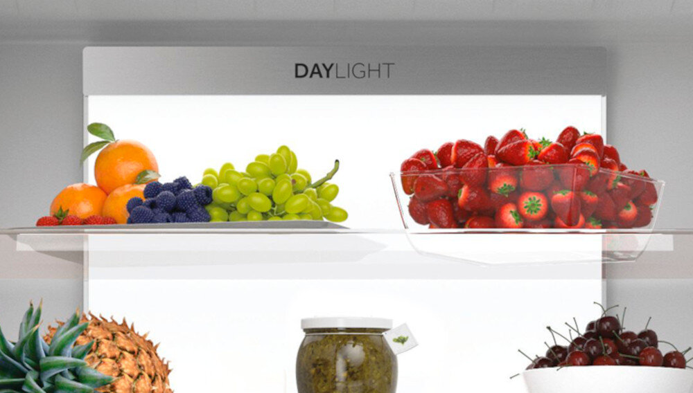Wnętrze lodówki z owocami na półkach, w tym pomarańcze, winogrona, truskawki i ananas. Widoczny napis \'DAYLIGHT\'.