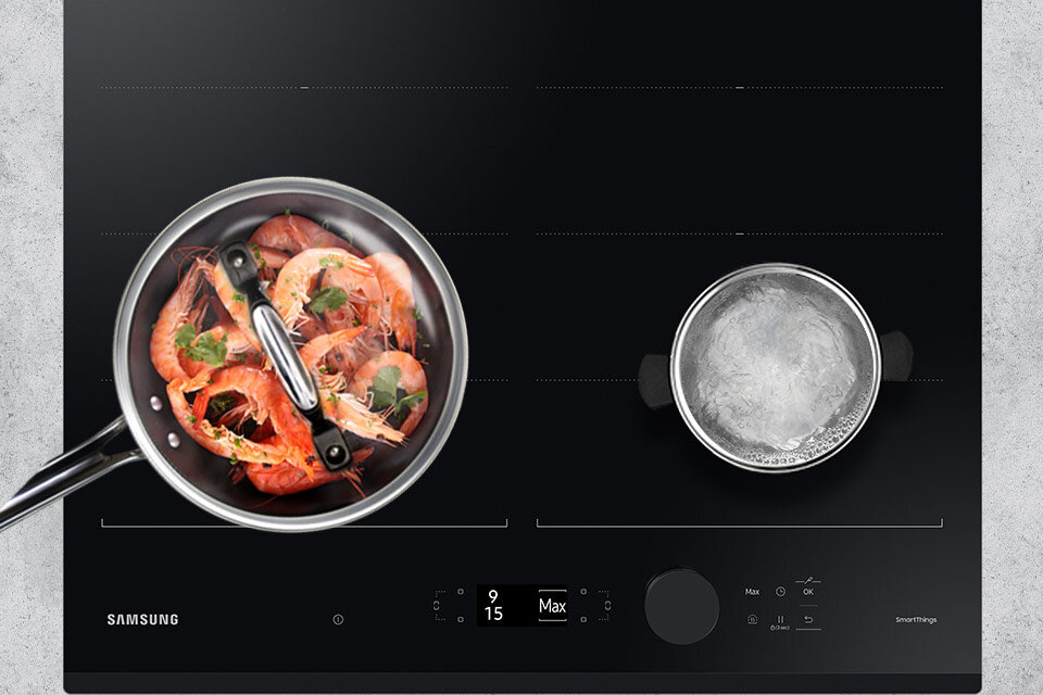 Czarna płyta indukcyjna z dwoma garnkami: jeden z krewetkami i ziołami, drugi z gotującą się wodą. Na płycie widoczne są napisy: \'SAMSUNG\', \'9\', \'15\', \'Max\', \'SmartThings\'.