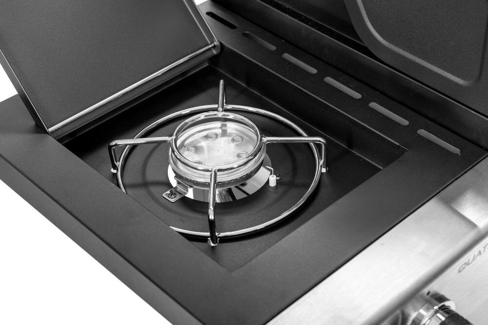 Zdjęcie przedstawia palnik boczny grilla gazowego z metalowym rusztem i pokrywą. W tle widoczna jest część obudowy grilla z metalowym wykończeniem.