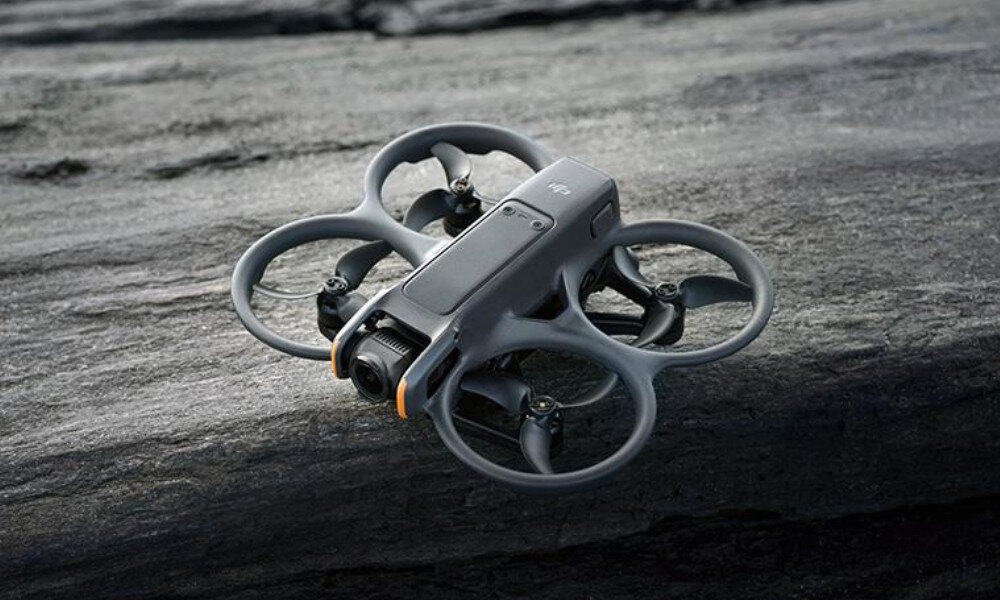 Na obrazie widoczny jest dron z czterema okrągłymi osłonami na śmigła, umieszczony na szarej, kamiennej powierzchni. Na górnej części drona znajduje się logo \'DJI\'.