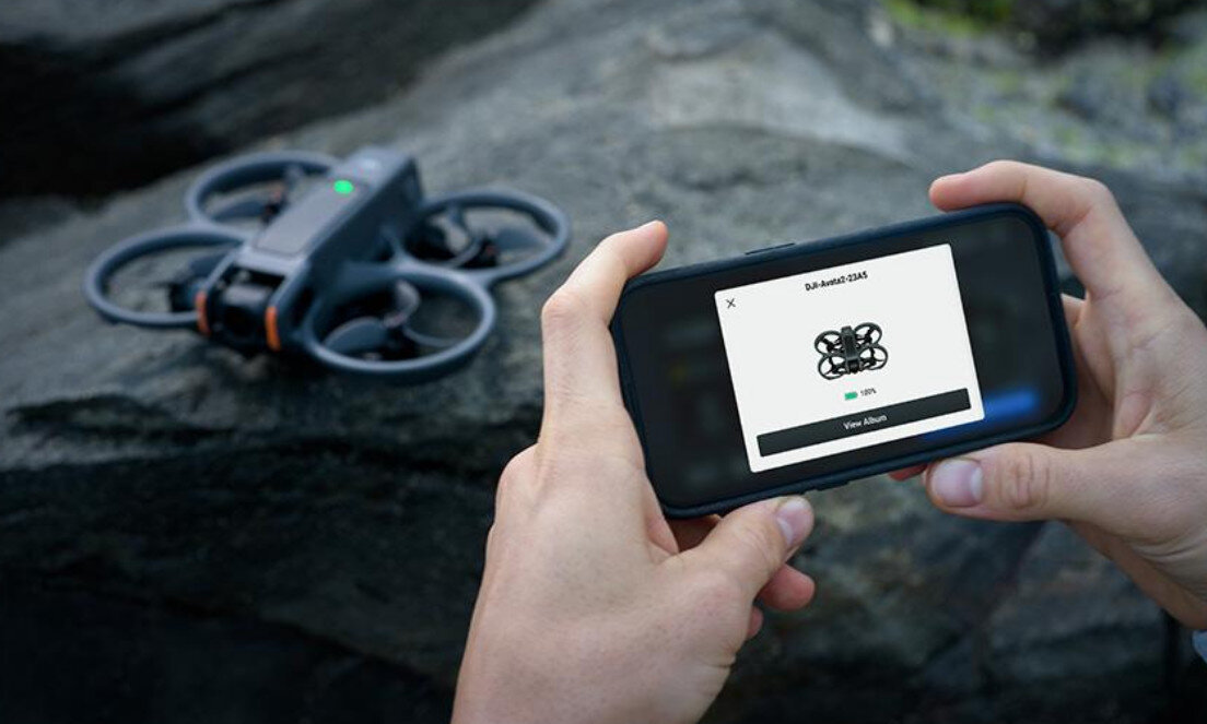 Osoba trzyma smartfon z wyświetlonym obrazem drona i napisem \'DJI Avata 2\'. Obok na skale znajduje się dron z widocznymi śmigłami i zielonym światłem.
