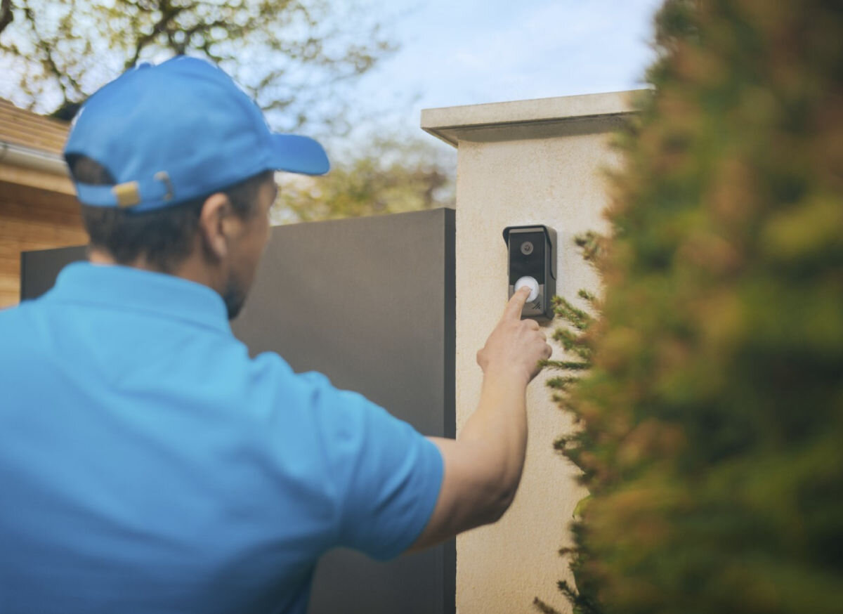 Zestaw wideodomofonowy SOMFY V350 Connect RTS Bezprzewodowy Wi-Fi, obraz, rozmowa, wideo, dźwięk, mężczyzna obsługuje panel zewnętrzny domofonu przy bramie wjazdowej