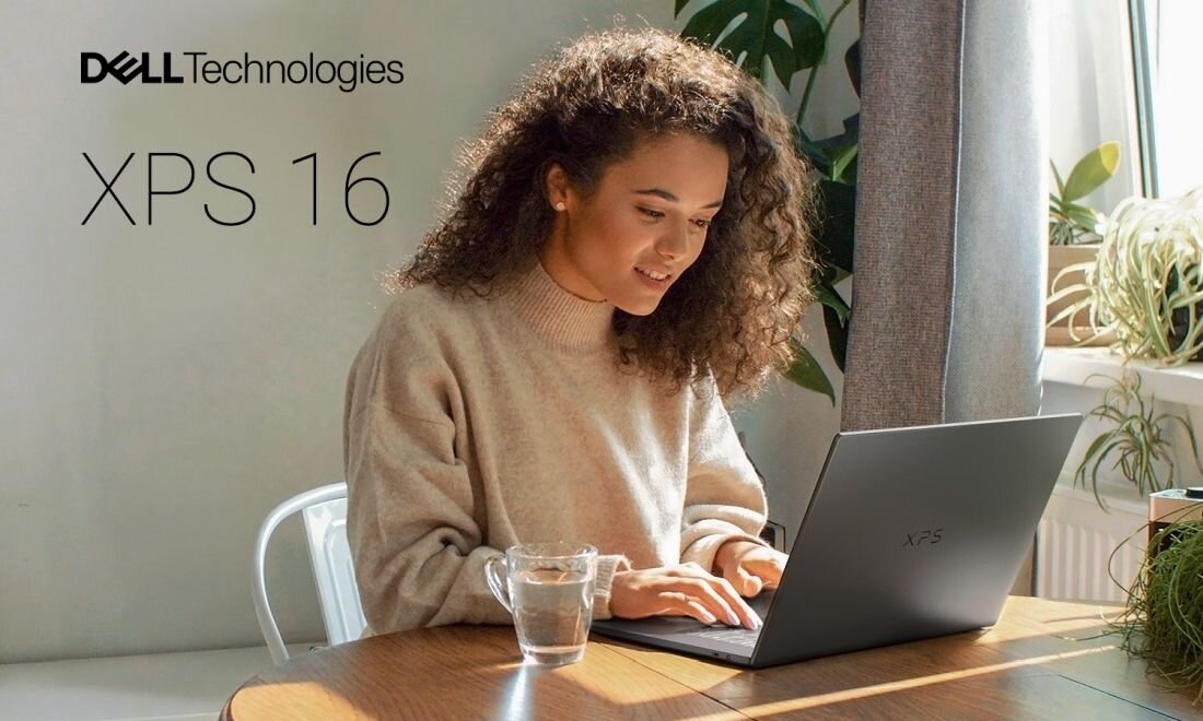 Osoba siedzi przy stole, używając laptopa marki DELL Technologies z napisem \'XPS 16\'. Na stole stoi szklanka z wodą, a w tle widać rośliny i zasłonę.