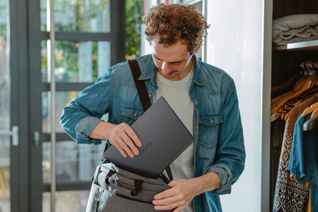 Osoba wkłada laptop Dell XPS 14 do torby podczas podróży, podkreślając mobilność i pracę na baterii  