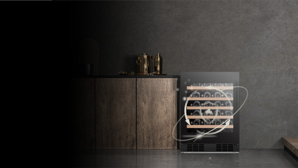 Na obrazie widoczna jest chłodziarka do wina z przeszklonymi drzwiami, w której widać ułożone butelki. Obok znajduje się drewniana szafka z dekoracjami na blacie.