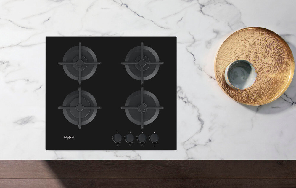 Czarna płyta gazowa z czterema palnikami i żeliwnymi rusztami, umieszczona na marmurowym blacie. Widoczne logo \'Whirlpool\' oraz cztery pokrętła do regulacji gazu.