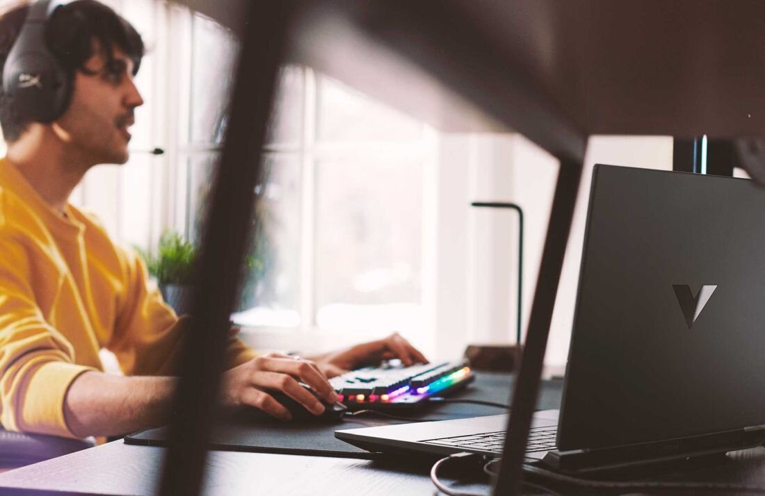 Laptop HP Victus 15 - Mężczyzna w słuchawkach siedzi przy biurku z laptopem, zaangażowany w aktywność związana z technologią. System audio DTS:X Ultra i HP Audio Boost 