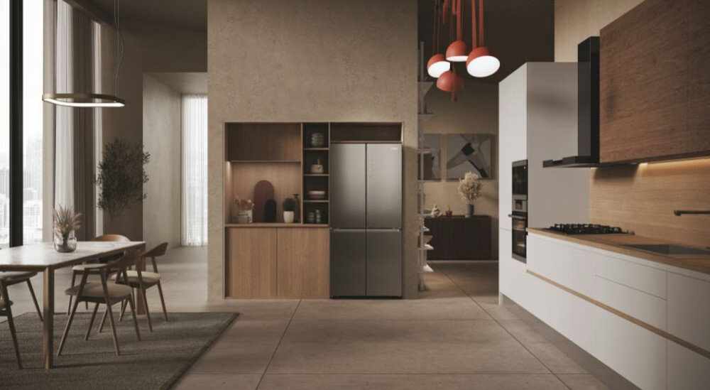 Nowoczesna kuchnia z lodówką w zabudowie, ciemny inox, otoczona drewnianymi szafkami. Wnętrze jest przestronne, z dużym stołem i wiszącymi lampami.