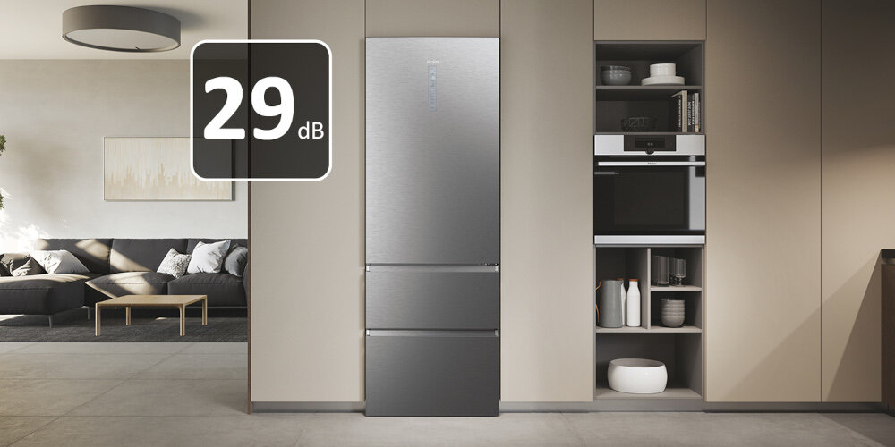 Wnętrze nowoczesnej kuchni z lodówką w kolorze platynowy inox, obok której znajduje się zabudowa z piekarnikiem i półkami. Na obrazie widoczny jest napis \'29 dB\'.