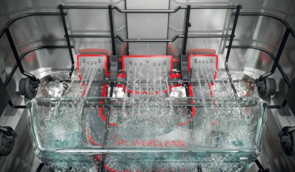 Wnętrze zmywarki z widocznymi strumieniami wody skierowanymi na naczynia. Na dnie zmywarki widoczny jest napis \'POWERCLEAN\'.
