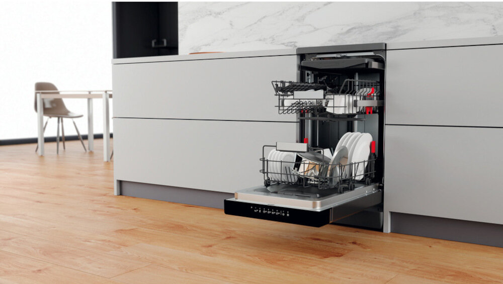 Zmywarka w zabudowie kuchennej z otwartymi drzwiami, ukazująca dwa poziomy koszy z naczyniami. Podłoga jest drewniana, a szafki mają jasnoszary kolor.