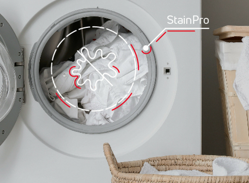 Otwarta pralka z widocznym bębnem pełnym białych ubrań, obok kosz na pranie. Na obrazie znajduje się napis \'StainPro\'.