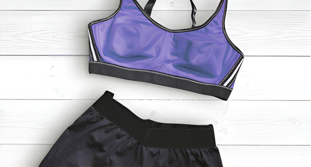 Na białym tle leży fioletowy sportowy stanik z czarnymi i białymi akcentami oraz czarne sportowe spodenki. Oba elementy odzieży są ułożone obok siebie.
