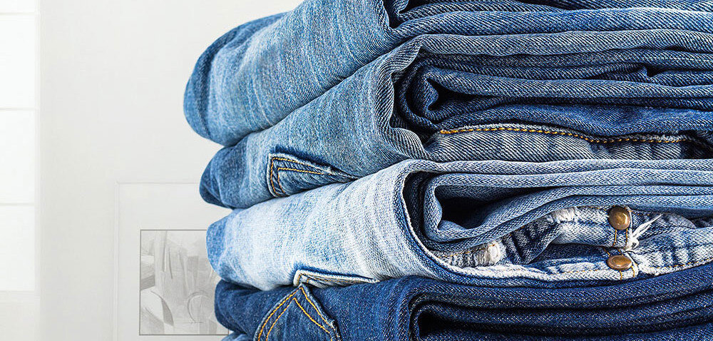 Stos złożonych jeansów w różnych odcieniach niebieskiego. W tle widoczna jest część ramki z obrazkiem.
