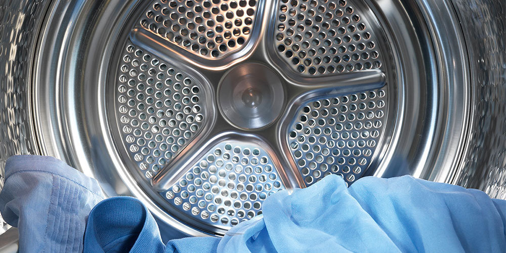 Wnętrze bębna pralko-suszarki z widocznymi metalowymi otworami i niebieskimi tkaninami w środku.