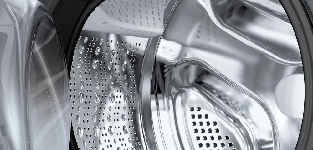 Zbliżenie na wnętrze bębna pralko-suszarki z widocznymi otworami w metalowej powierzchni.