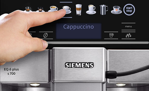 Osoba dotyka panelu dotykowego ekspresu do kawy, na którym wyświetla się napis \'Cappuccino\'. Widoczne jest logo \'SIEMENS\' oraz oznaczenie modelu \'EQ.6 plus s700\'.