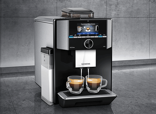 Ekspres do kawy z wyświetlaczem pokazującym opcje napojów, z logo SIEMENS na froncie. Na tacy znajdują się dwie filiżanki z kawą.