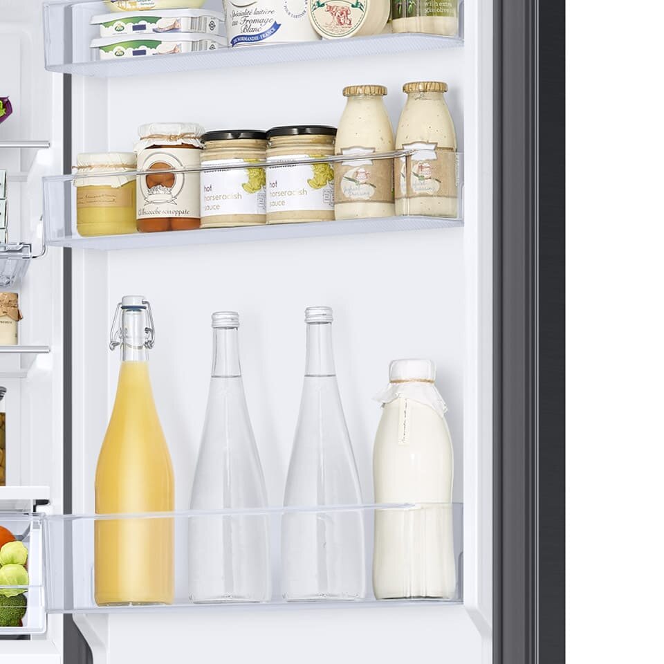 Głębokie pojemniki na drzwiach pomieszczą słoiki i butelki Wnętrze drzwi lodówki z półkami wypełnionymi różnymi produktami spożywczymi, w tym butelkami i słoikami. Na górnej półce znajdują się słoiki z sosami i przetworami, a na dolnej butelki z napojami.