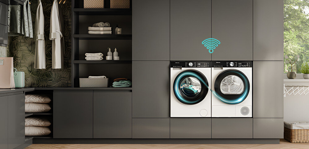 W nowoczesnej pralni znajdują się pralka i suszarka w zabudowie, z ikoną Wi-Fi nad nimi. Obok widoczne są półki z ubraniami i akcesoriami do prania.