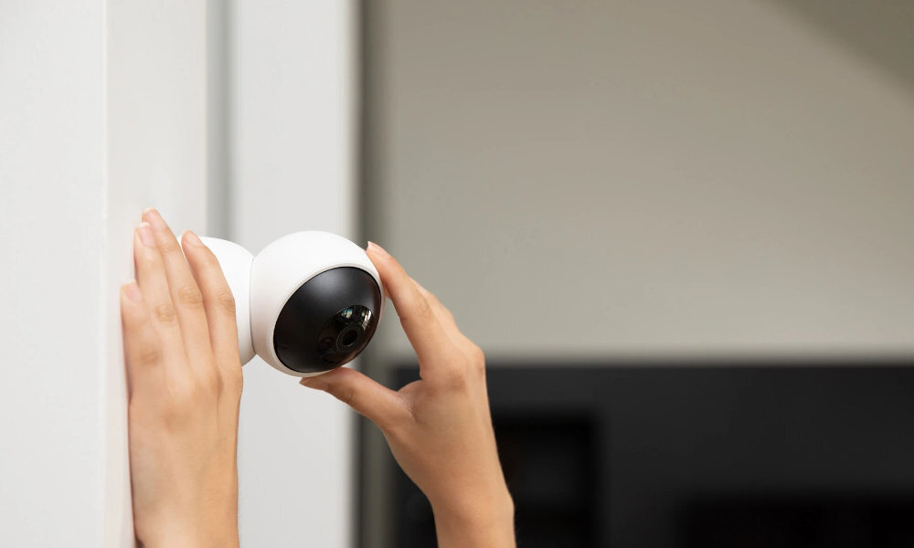 Osoba montuje białą, obrotową kamerę na ścianie. Kamera ma czarny, wypukły obiektyw.